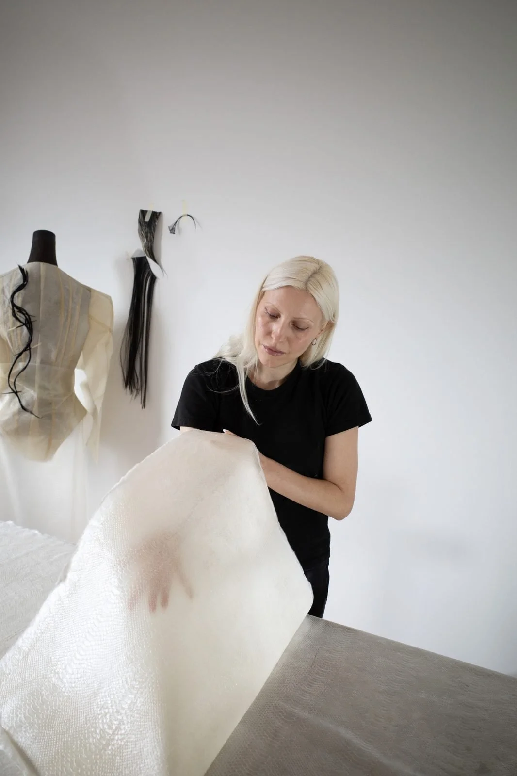Janine Grosche lifting a large handmade translucent snake skin latex sheet during the material development process for PATH.