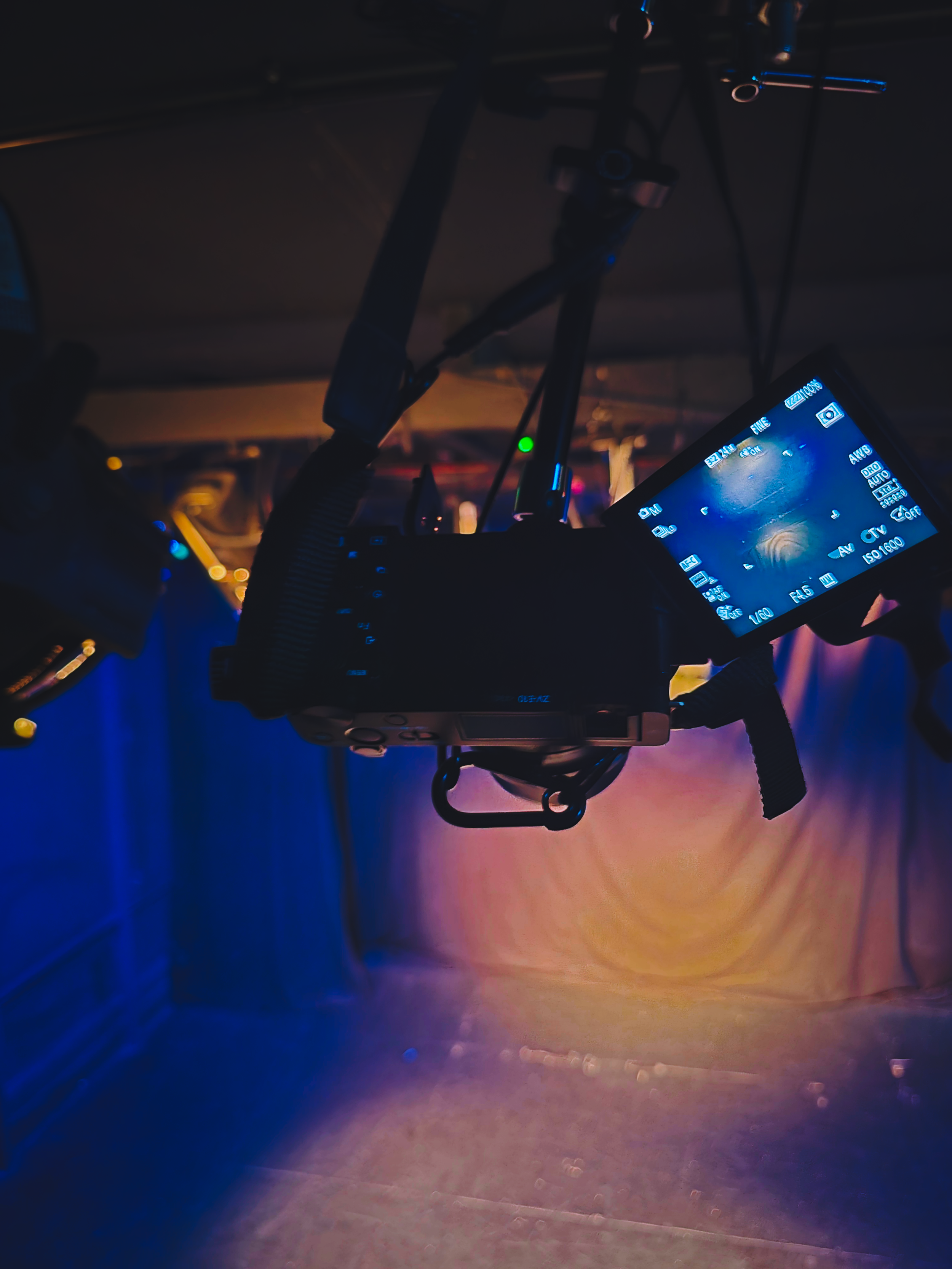 A professional camera with a large display screen, mounted on a tripod, in a dimly lit indoor environment with purple and blue lighting.