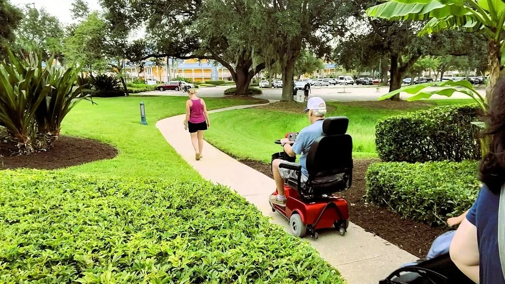 The picture shows a winding path to the parking lot and resort at Caribbean Beach. A man is navigating it with a mobility scooter.