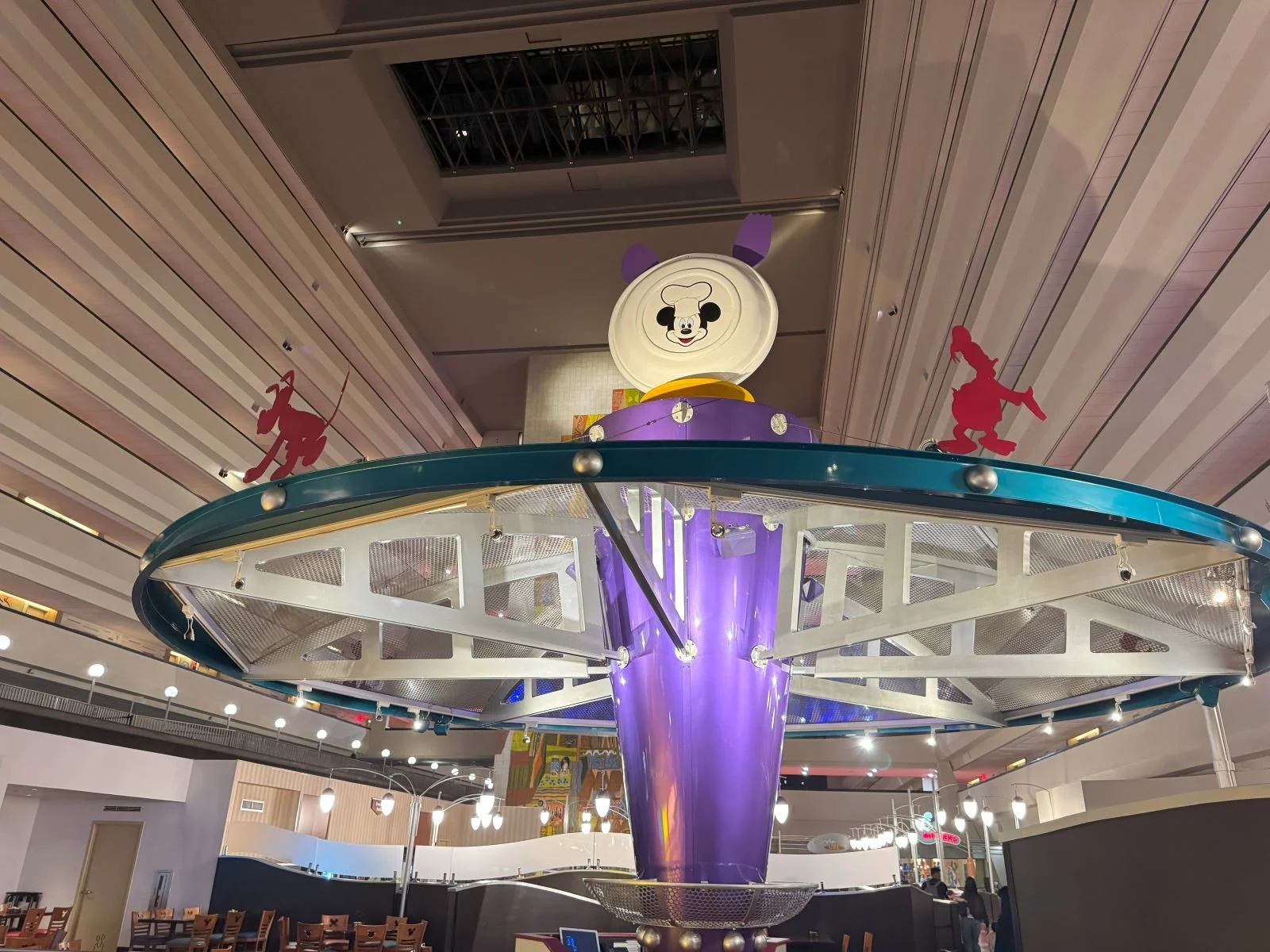 A picture of the decorative covering at Chef Mickey's. Character silhouettes surround a giant plate with Mickey's face on it. You can see the many stories of the Contemporary resort and the monorail track in the background.