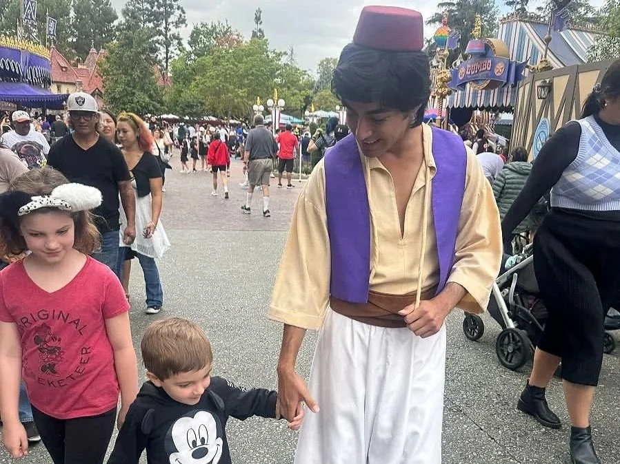 A picture of a cast member dressed as Aladdin holding hands with a small boy in Fantasyland. Disneyland California Anaheim.