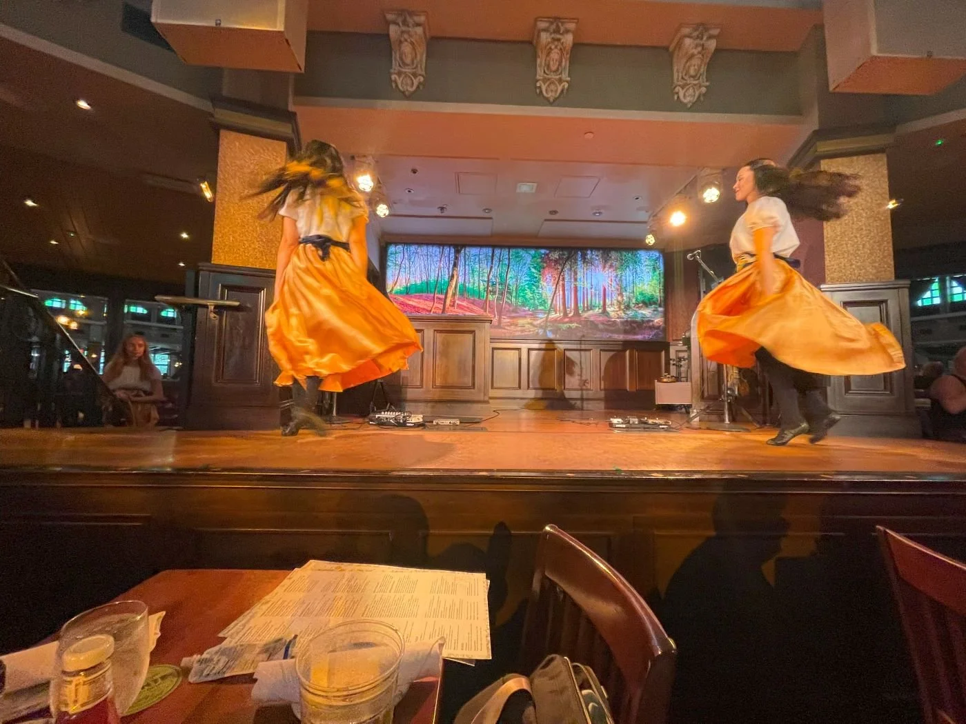 Two women in orange skirts tap dance on the stage at Raglan Road, an irish restaurant in Disney Springs at Disney World. Another waits in the wings. A great restaurant for kids at Disney World.
