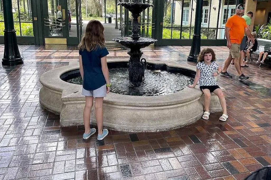The central part of the port orleans french quarter lobby has an indoor fountain. Two girls stand near it while others walk around.