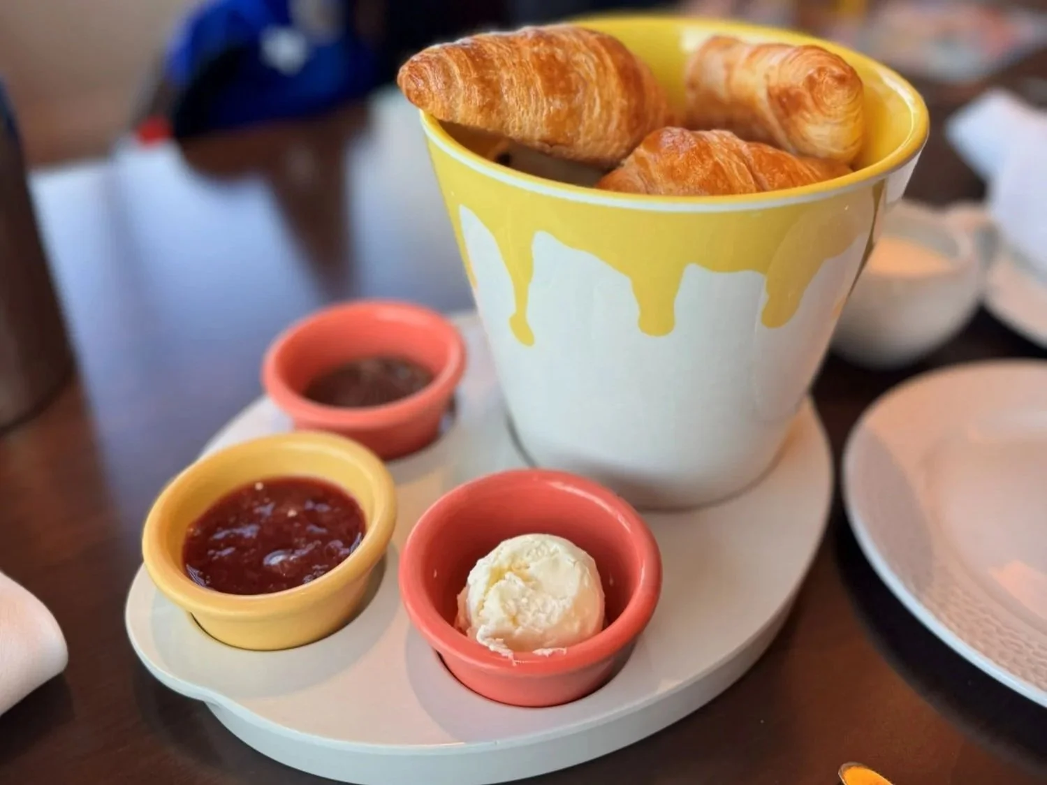 A photo of a bucket of pastries at Topolino's character meal. The bucket is a paint bucket with honey butter, strawberry jam, and chocolate hazelnut spread around it.