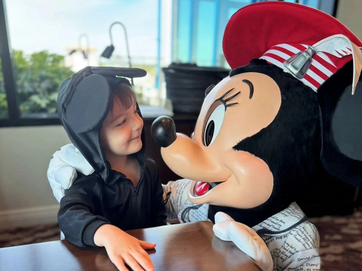 Minnie mouse nose to nose with a toddler boy in a Mickey costume at Topolino's Character breakfast at Walt Disney World's Riviera Resort. The boy is making a cute smirk and looking at poet minnie.