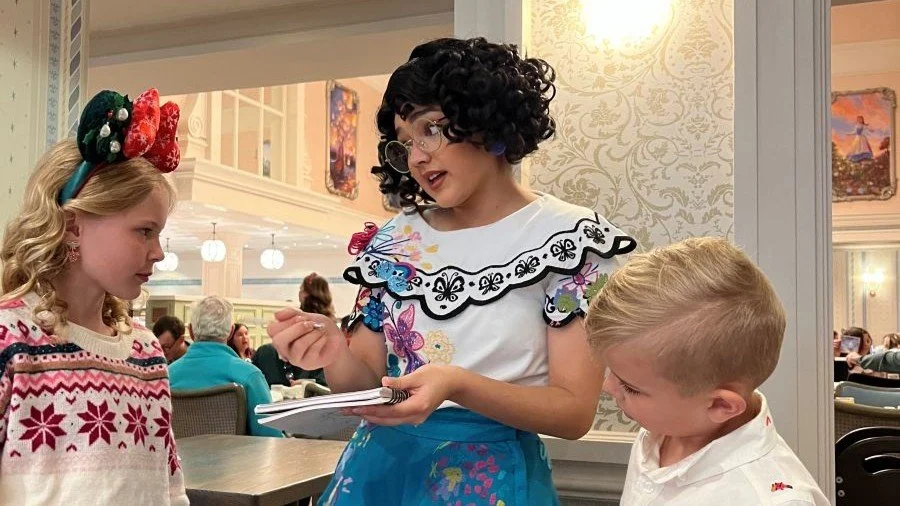 Mirabel from Encanto talks to a brother and sister while signing an autograph book. At 1900 Park Fare in Disney's Grand Floridian Resort.