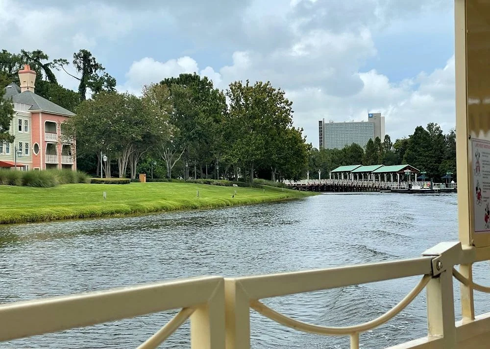 A view of a coral Saratoga Springs building and the Disney Springs dock from a boat railing. The boat is coming from Disney Springs to Port Orleans.