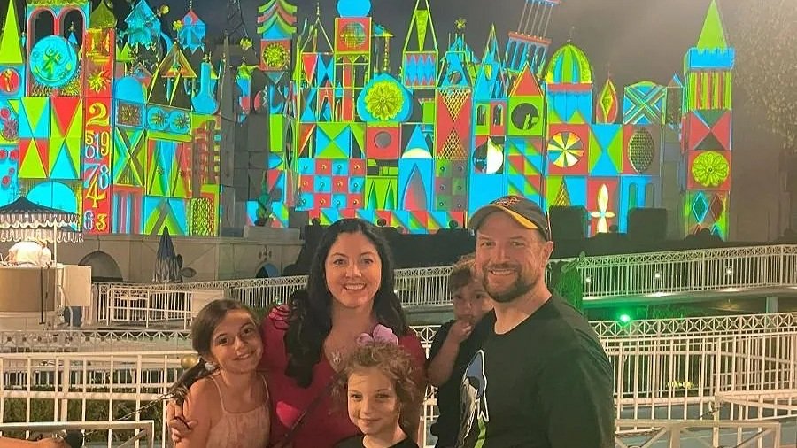 a family stands in front of the it's a small world facade at night. The decorations are lit up in red blue and green.
