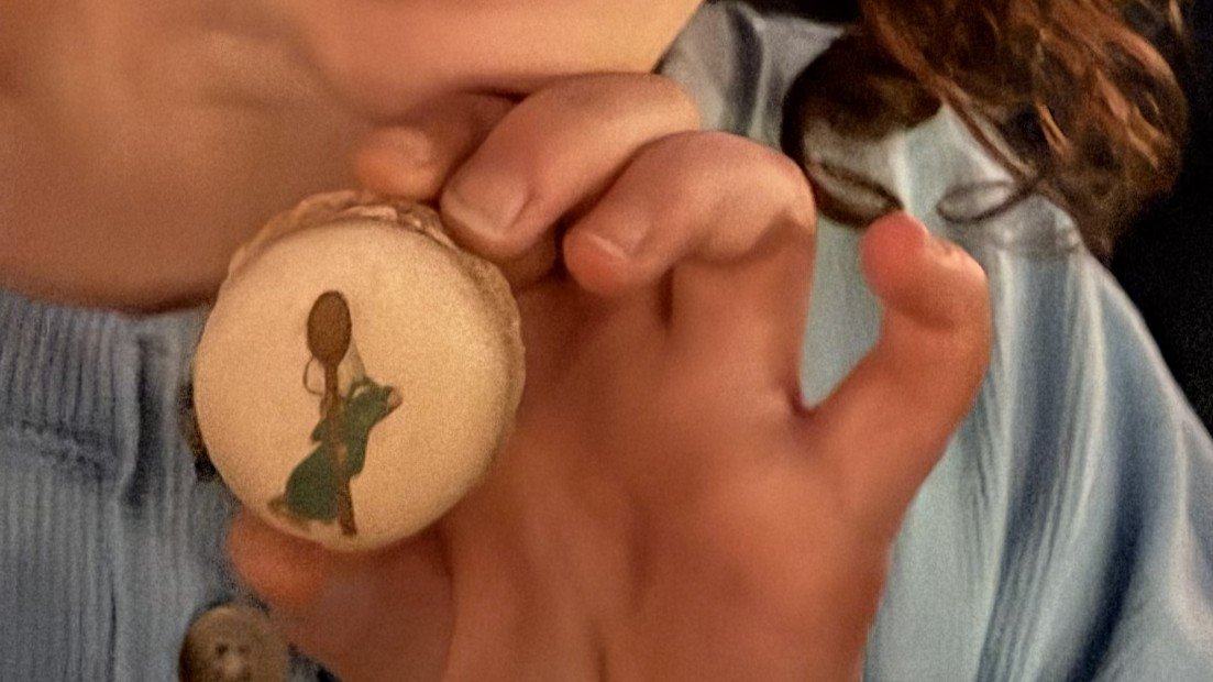 A little girl holds up a beige macaron with a picture of Remy from Ratatouille on it. From Disneyland Paris.