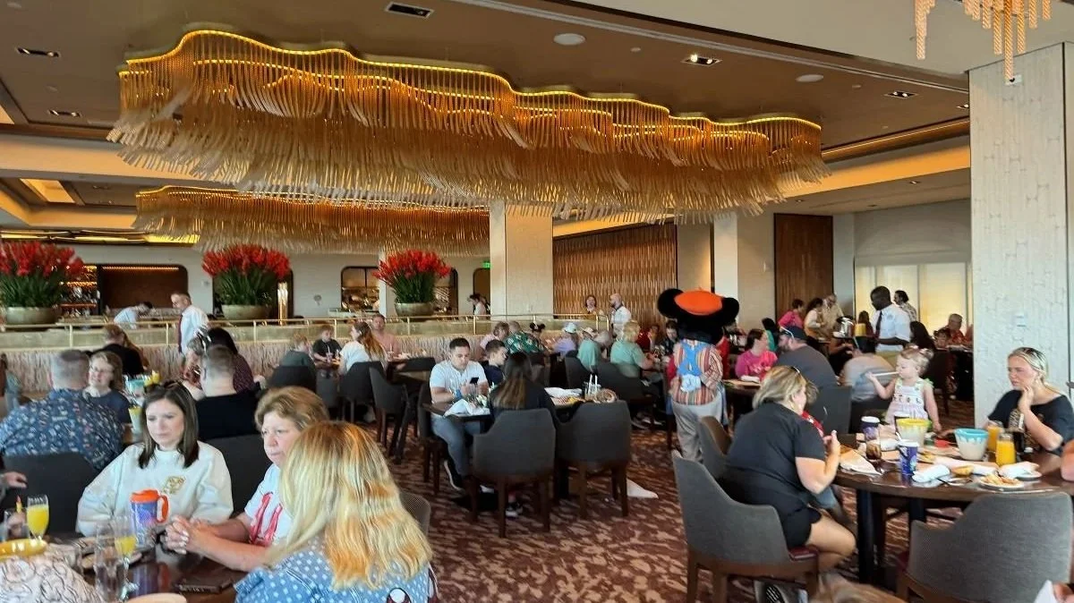 The dining room at Topolino's in the Riviera Resort. You can see intricate chandeliers in the ceiling and painter Mickey's back as he interacats with guests.