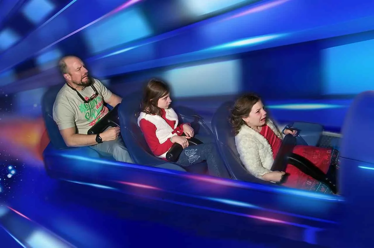 A dad, a 9 year old daughter and a 7 year old daughter make crazy faces riding Space Mountain at Disney World's Magic Kingdom. They are wearing Christmas clothes.
