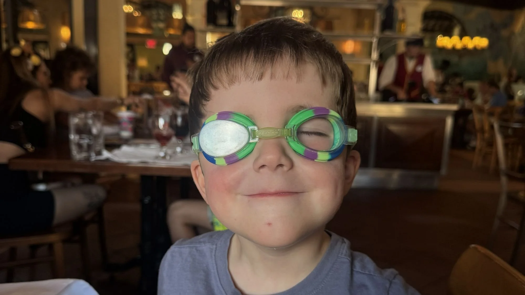 A toddler poses for the camera wearing swim goggles at Via Napoli in EPCOT at Disney World. A great Disney restaurant for children.