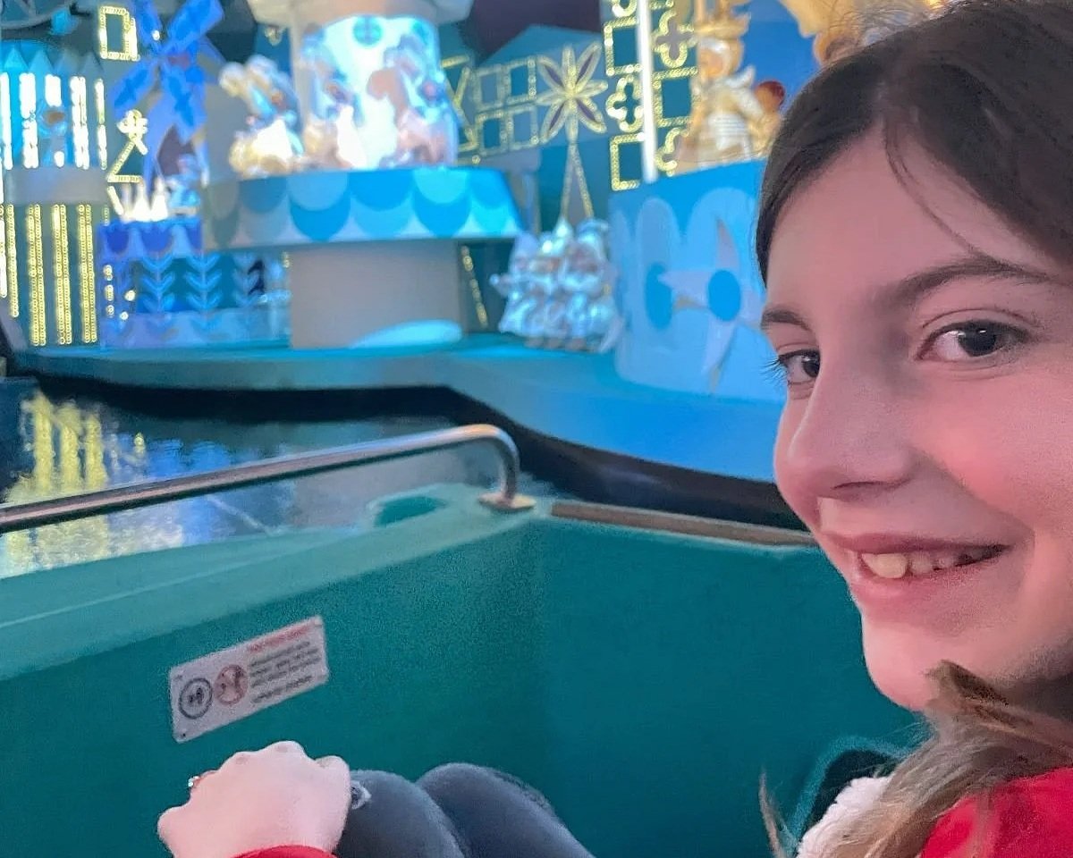 A 9 year old girl smiles back at the camera in the final scene of Disney World's it's a small world, where all of the characters are wearing white.