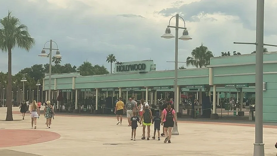 a photo of the entrance of hollywood studios, you can see people walking towards the multiple metal detectors and ticket scanners under the aqua awning