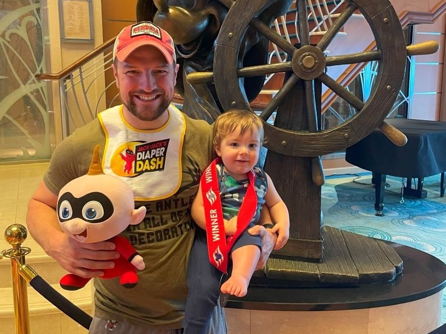 My son and I standing in front of the atrium statue of Mickey as a sailor on the Disney Magic. He is wearing a medal because he just won the Jack Jack's Diaper Dash.