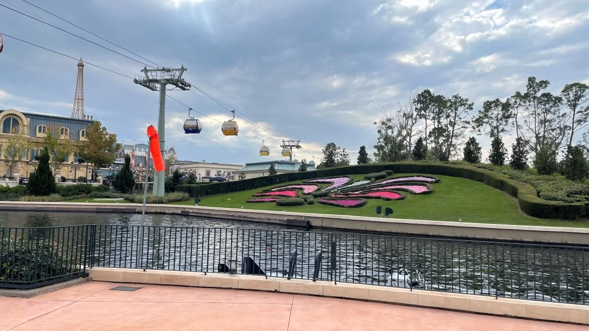 A balcony overlooking the waterway in epcot at the international gateway. You can see a fleur de lis in the garden, with the skyliner gondolas overhead. Epcot's France pavilion is to the left with the eiffel tower. Disney skyliner goes to riviera