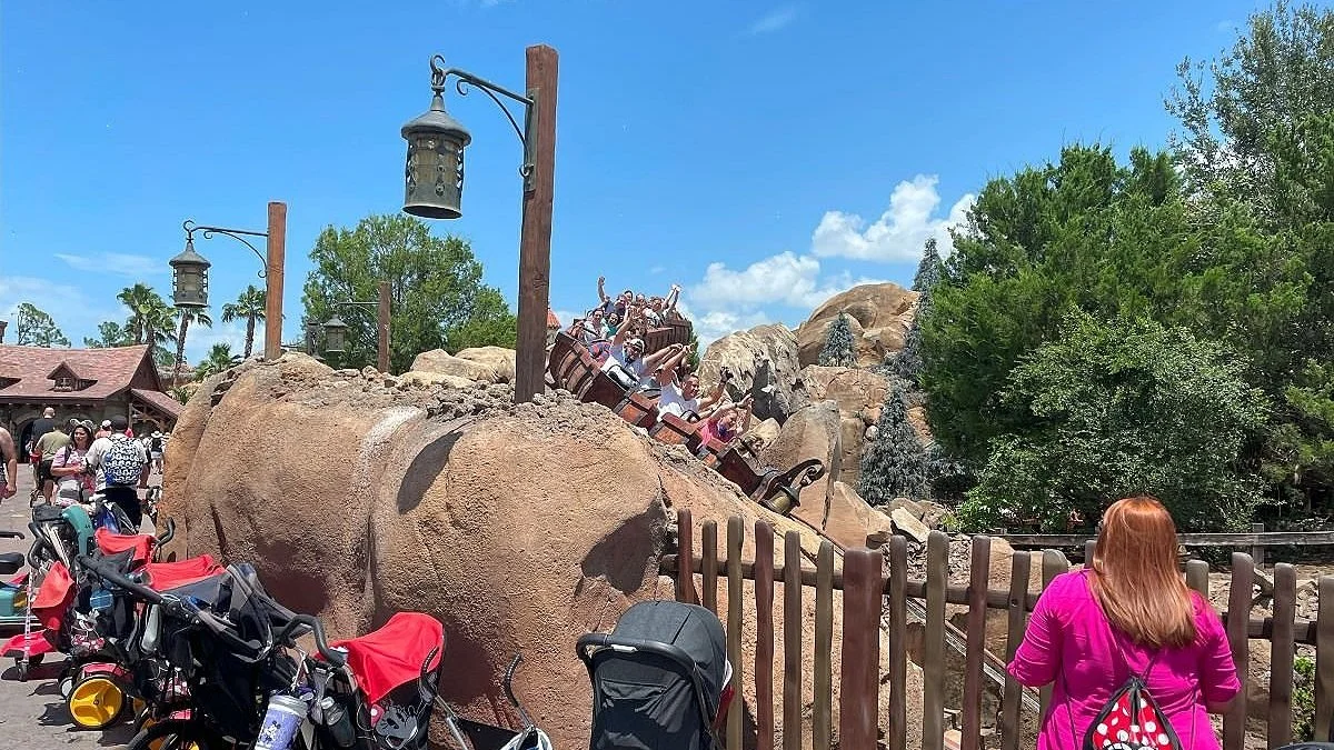 An image of the Seven Dwarfs Mine train at Disney World in Orlando. You can see guests raising their hands as they come around the roller coaster turn. On the left, there are lots of strollers.
