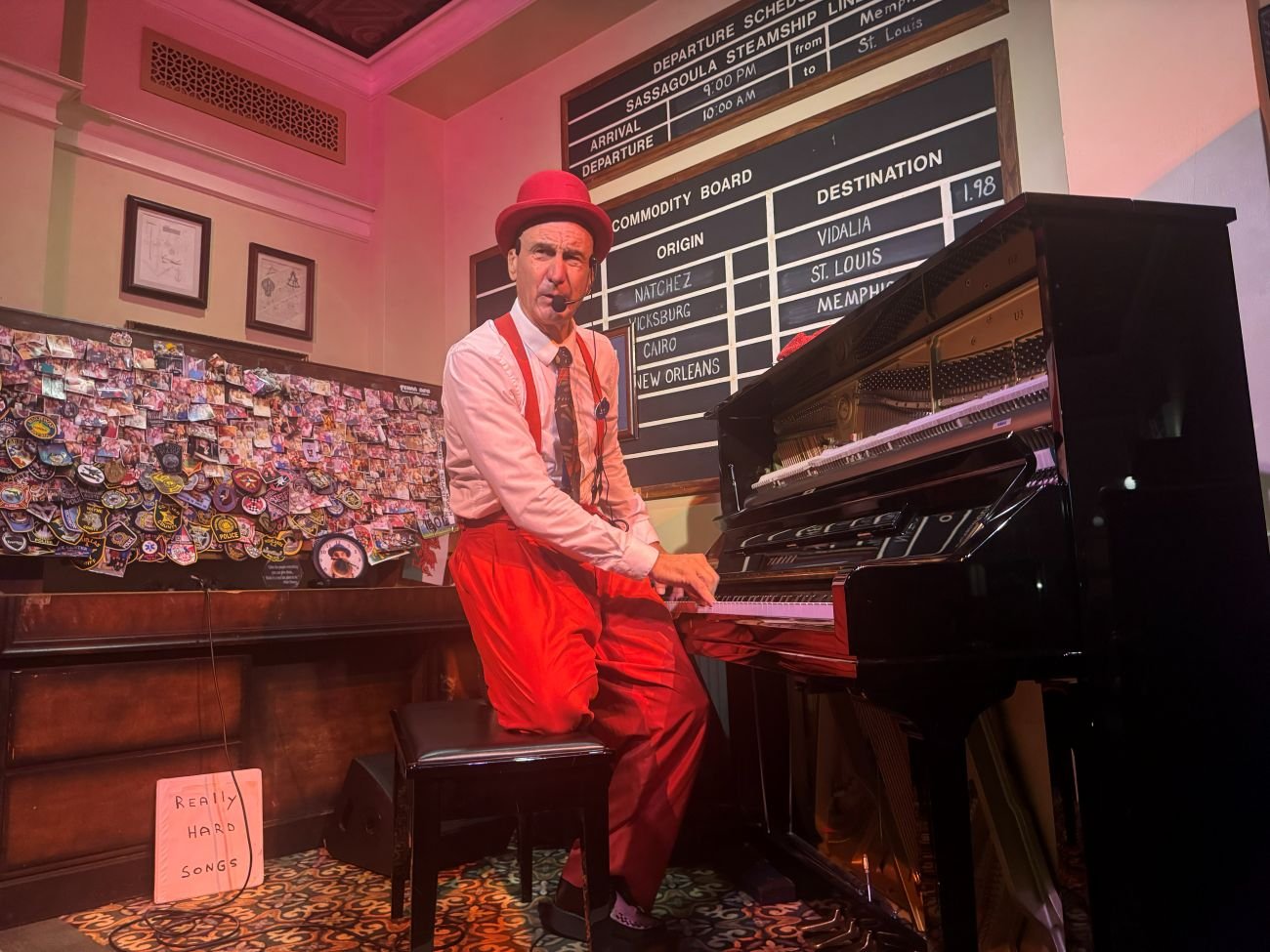 A man in a bowler hat and matching oversized pants held up by suspendes plays a custom piano while sitting on one knee. Yehaa Bob show at Port Orleans Riverside, a moderate Disney resort.