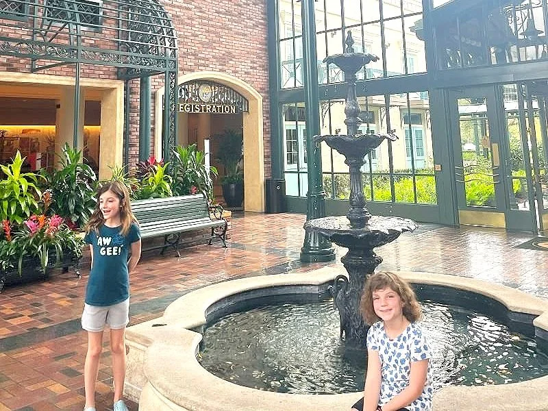 Two girls smile at the fountain in the lobby of Port Orleans French Quarter, which is a good stop if you're heading from a Disney park to Disney Springs