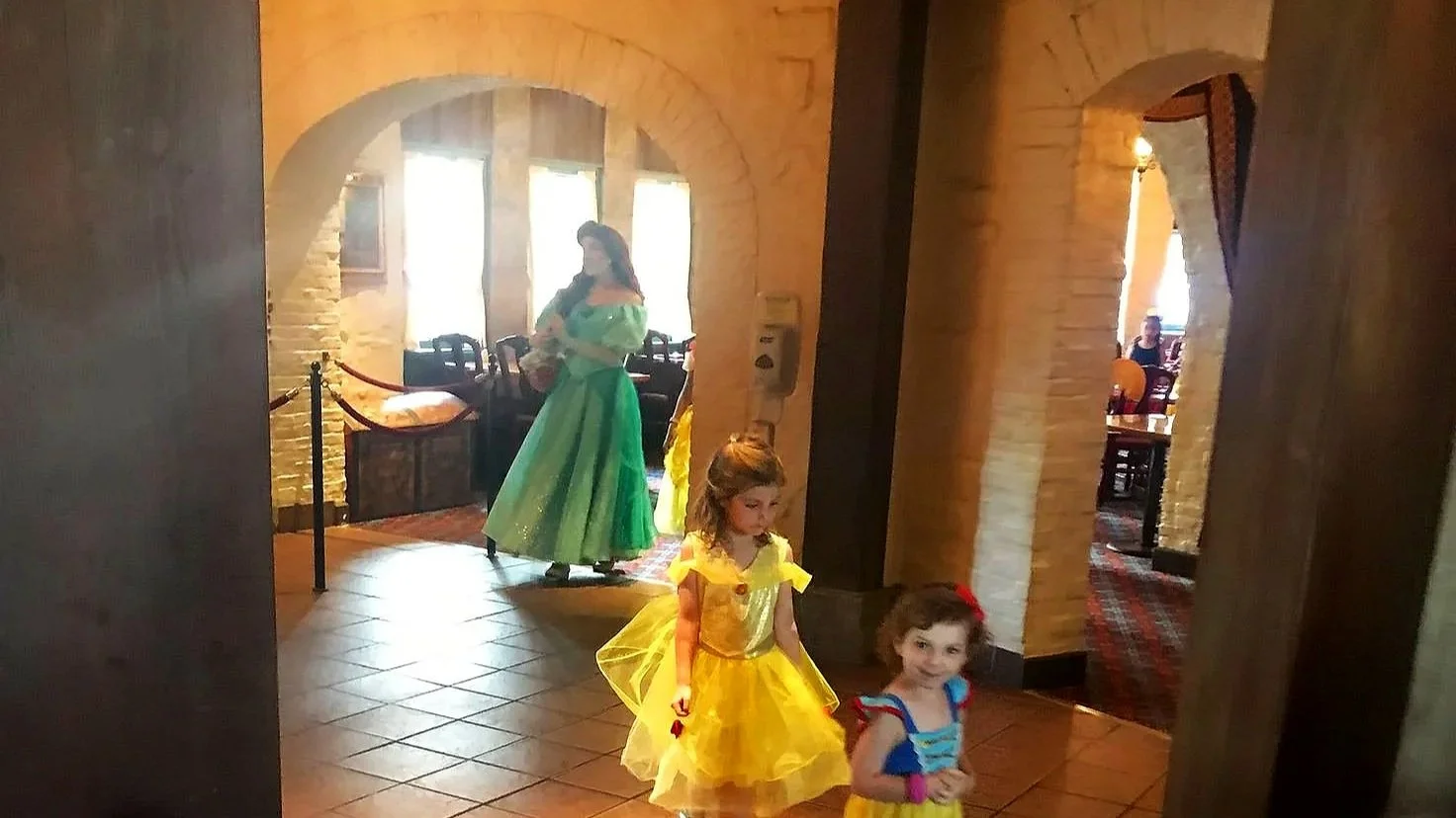 Two girls walk past Ariel at Akershus in EPCOT. You can see the stone arches and rectangular timber columns.