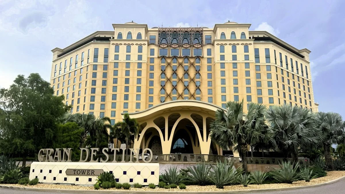 The entrance to coronado springs resort at Disney World, the gran destino tower. You can see the sign in fron tof the tower, and the intricate design of the carport, the crisscross design going up the center of the tower. With lots of palm trees