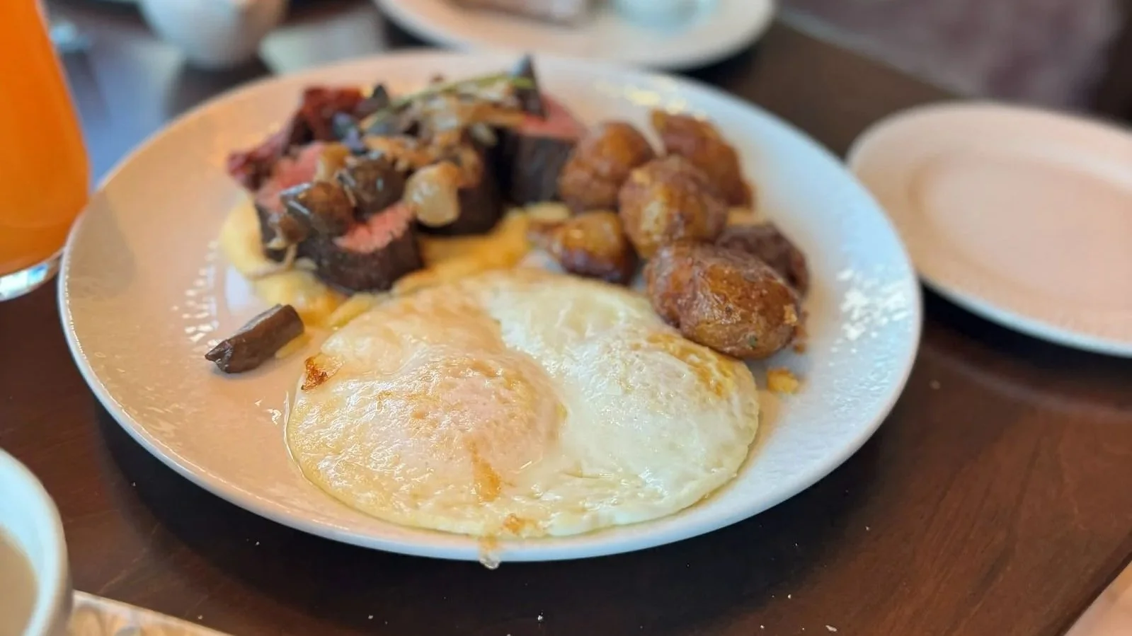 The wood fired steak and eggs at Topolino's character breakfast in Riviera Resort at Disney World. You can see two fried eggs, potatoes, and slices of steak.