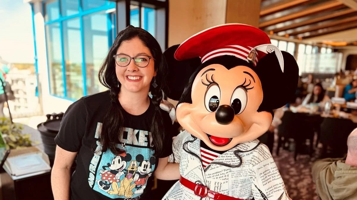 A lady with a Mickey Mouse shirt poses with Minnie Mouse dressed as a poet at Topolino's character breakfast in Disney's Riviera Resort at Walt Disney World.