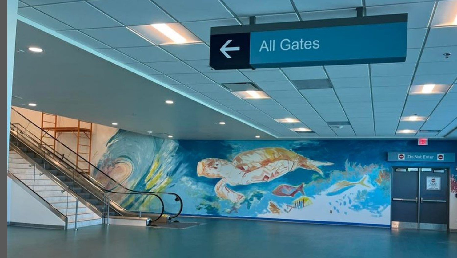 A new area that's part of a Melbourne International Renovation. It's an underwater watercolor mural prominently featuring a sea turtle. There's an escalator for airline passengers to the left and a sign that says all gates who are leaving from MLB