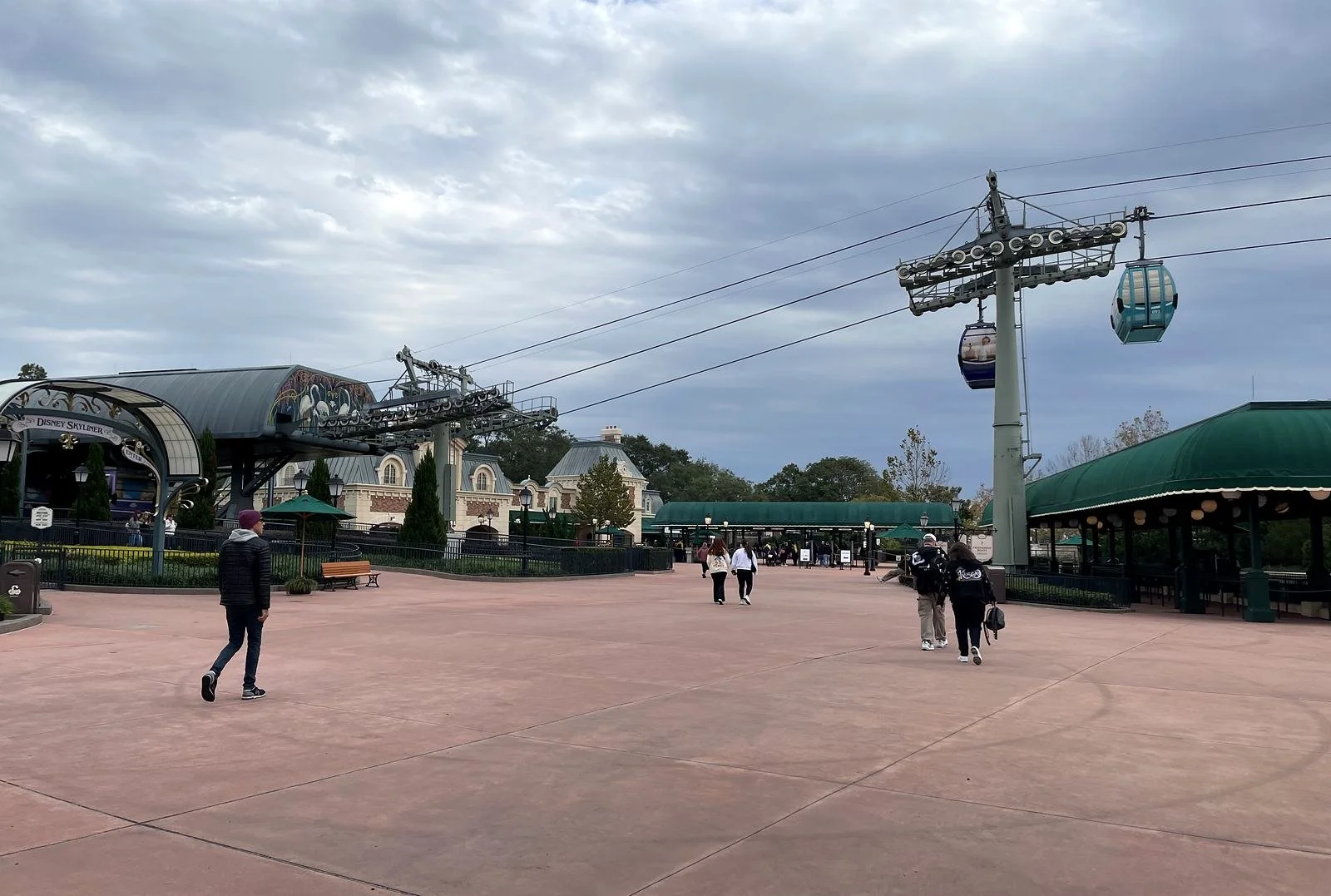 A photo of the international gateway at epcot in Disney World. You can see lots of green awnings and the Skyliner station with several gondolas. A few people are walking towards the park.