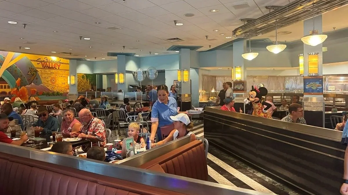 The dining room of Hollywood and Vine, character dining at Hollywood Studios. You can see basic drop ceiling, a mural of classic hollywood, and leather booths with stainless steel frames. The lighting near the buffet has classic diner chrome touches.