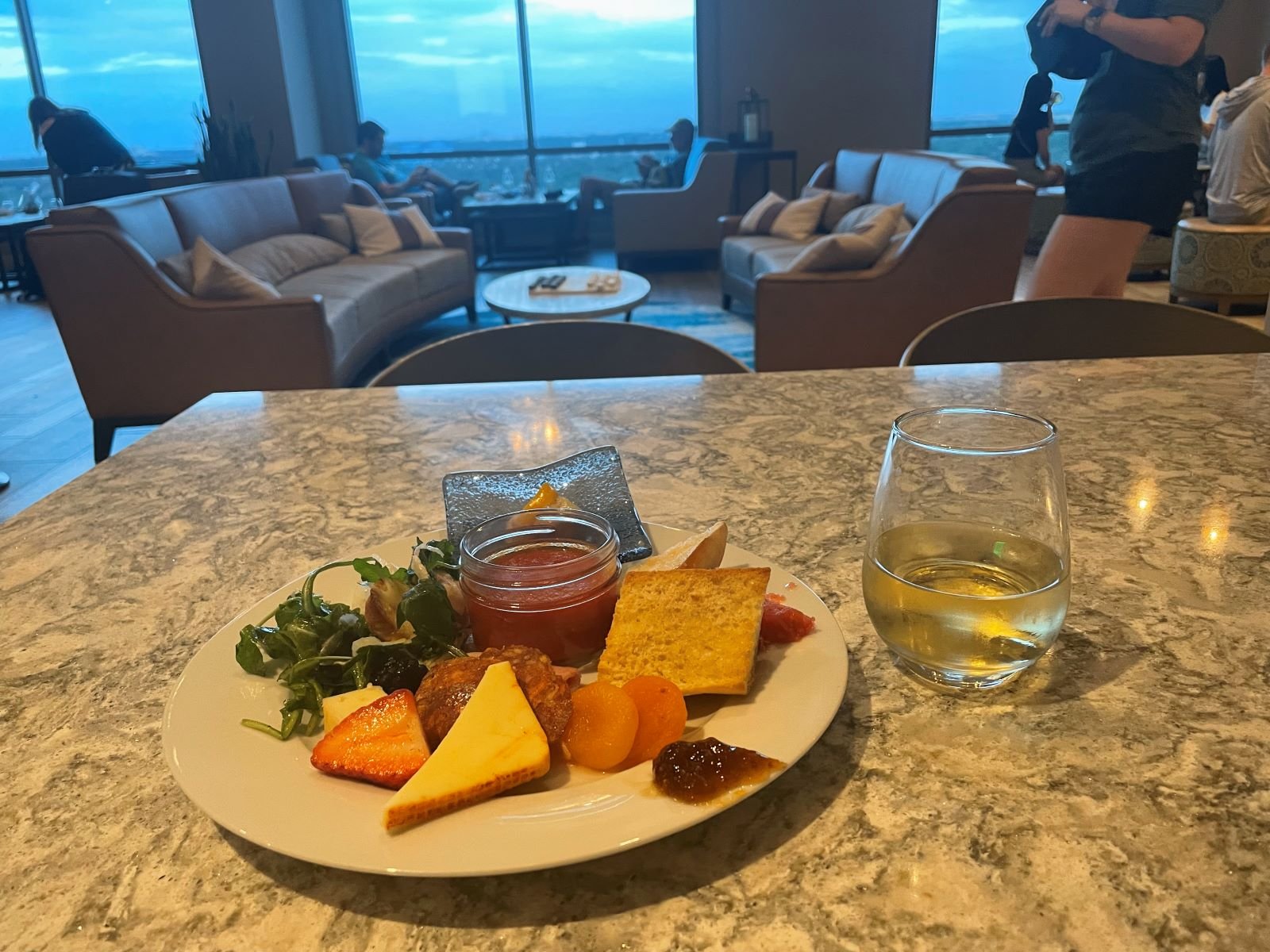 An image of the Chronos Club lounge in Coronado Springs, a moderate resort at disney world. Foreground: charcuterie plate on a marble table. background couches and tables overlooking hollywood studios