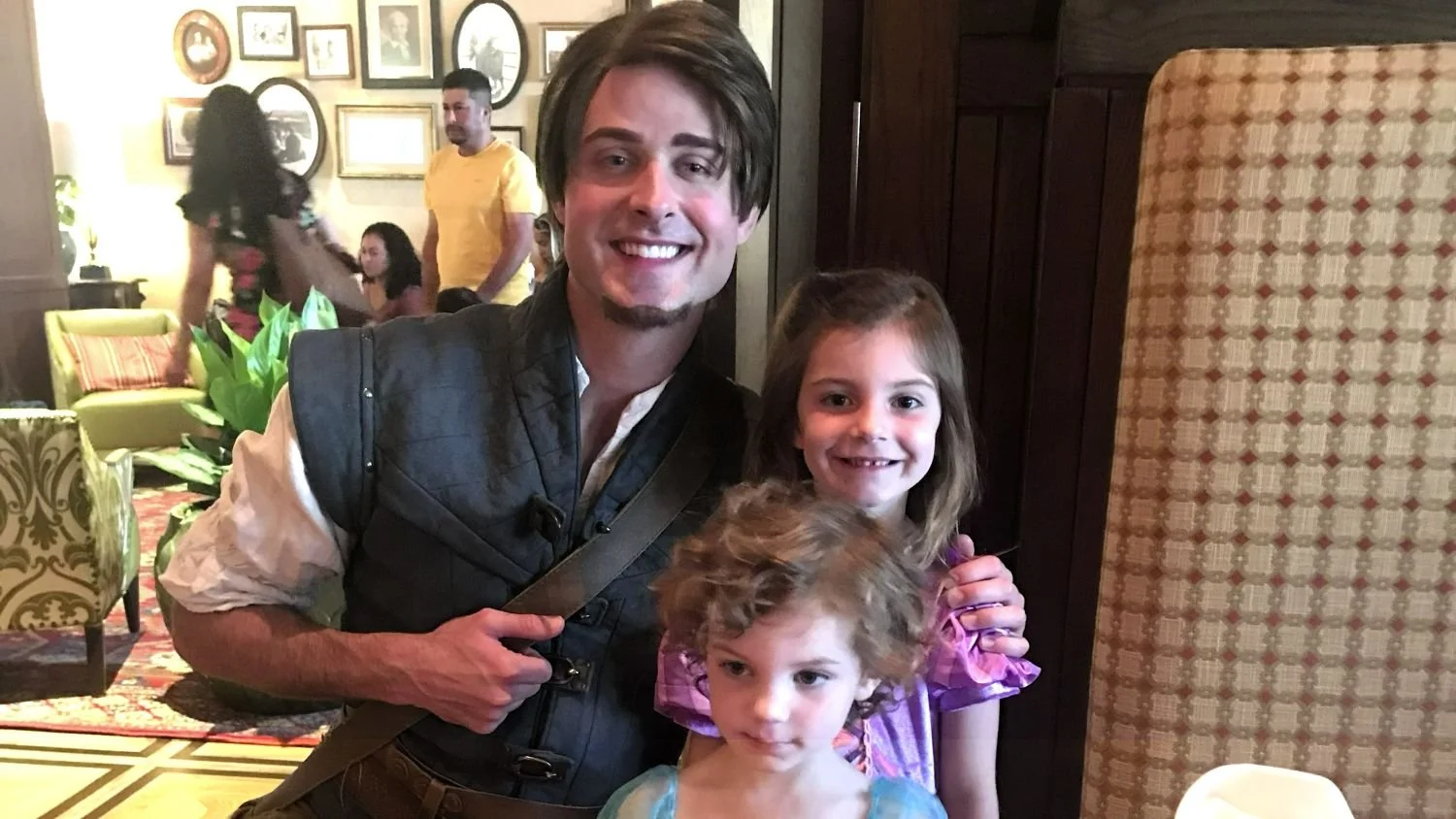 Two girls in Disney princess dresses pose with Flynn Rider at Trattoria al Forno, one of Disney World's character dining experiences. This one hasn't reopened since covid.