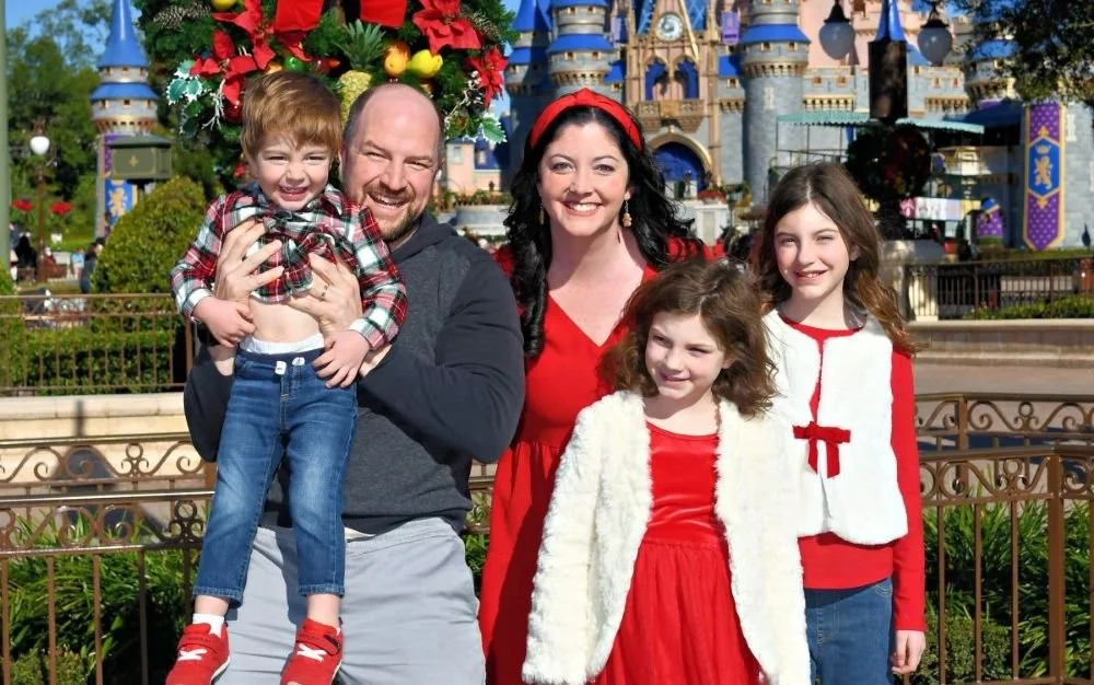 A family poses in front of the Walt Disney World castle with christmas clothes on. It's november and they are warmly dressed.