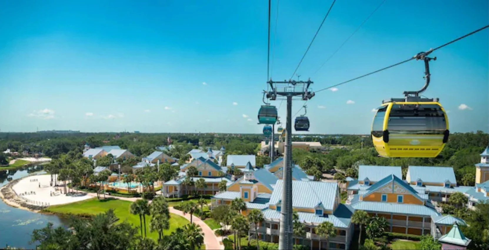 A picture from the skyliner into caribbean beach resort. You can see several yellow buildings with blue roofs, a beach area, and the pool at this moderate resort in Disney World.