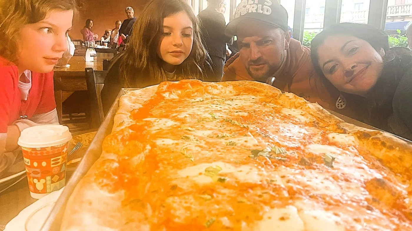 A family posing behind an enormous cheese pizza at Via Napoli, an Italian restaurant in the Italy pavilion in EPCOT at Disney World.