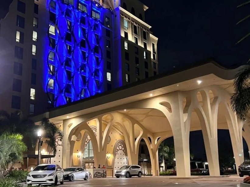 An image of the entrance of coronado springs gran destino tower at night. You can see the oversized carport with eccentric shapes and blue lighting going up the tower. Several cars parked out front.