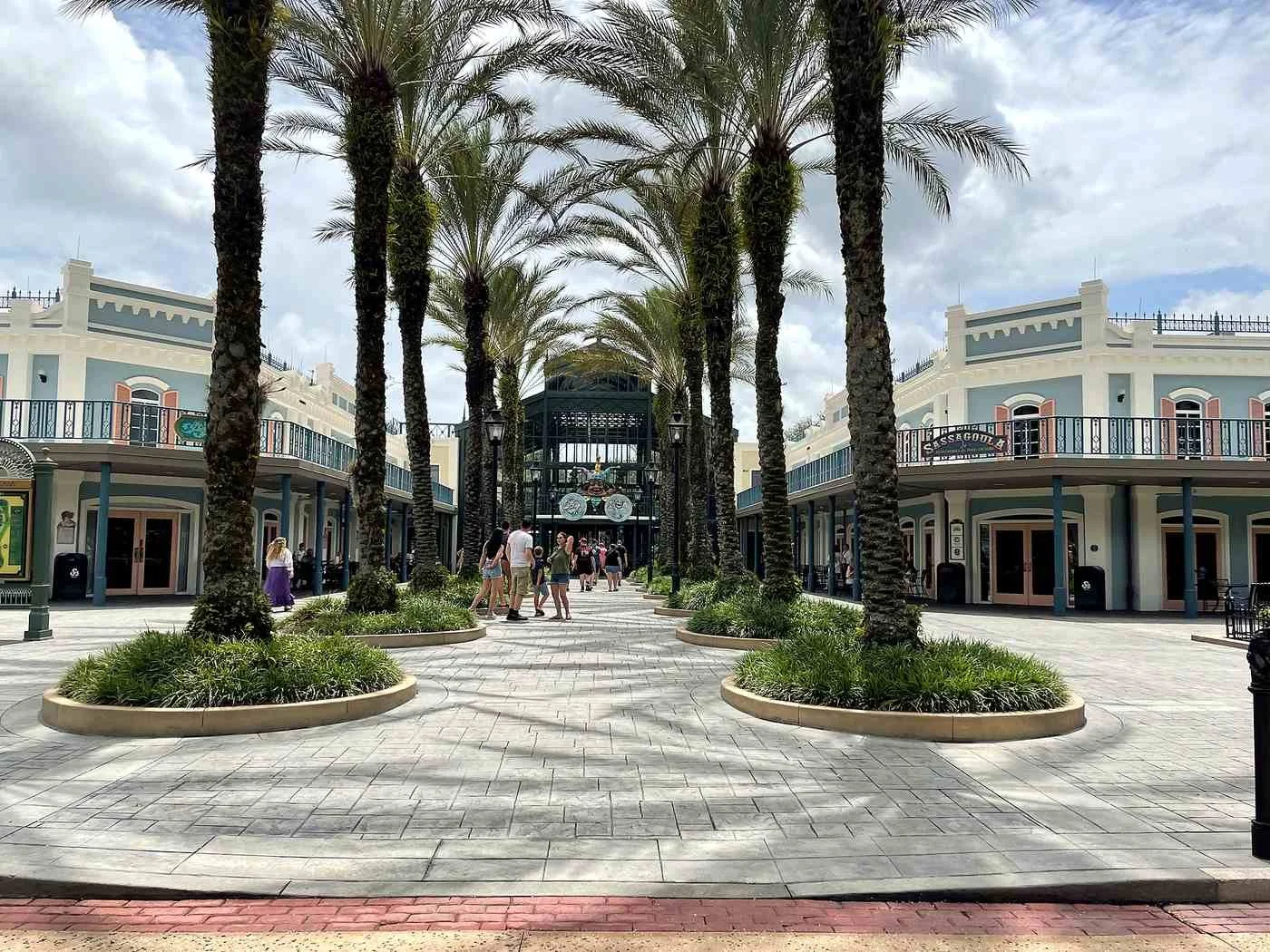 A photo of the backside of the French Quarter lobby, a moderate resort at Disney World. Palm tree planters lead to the entrance, which has mardi gras decorations and lots of wrought iron reminiscent of New Orleans.
