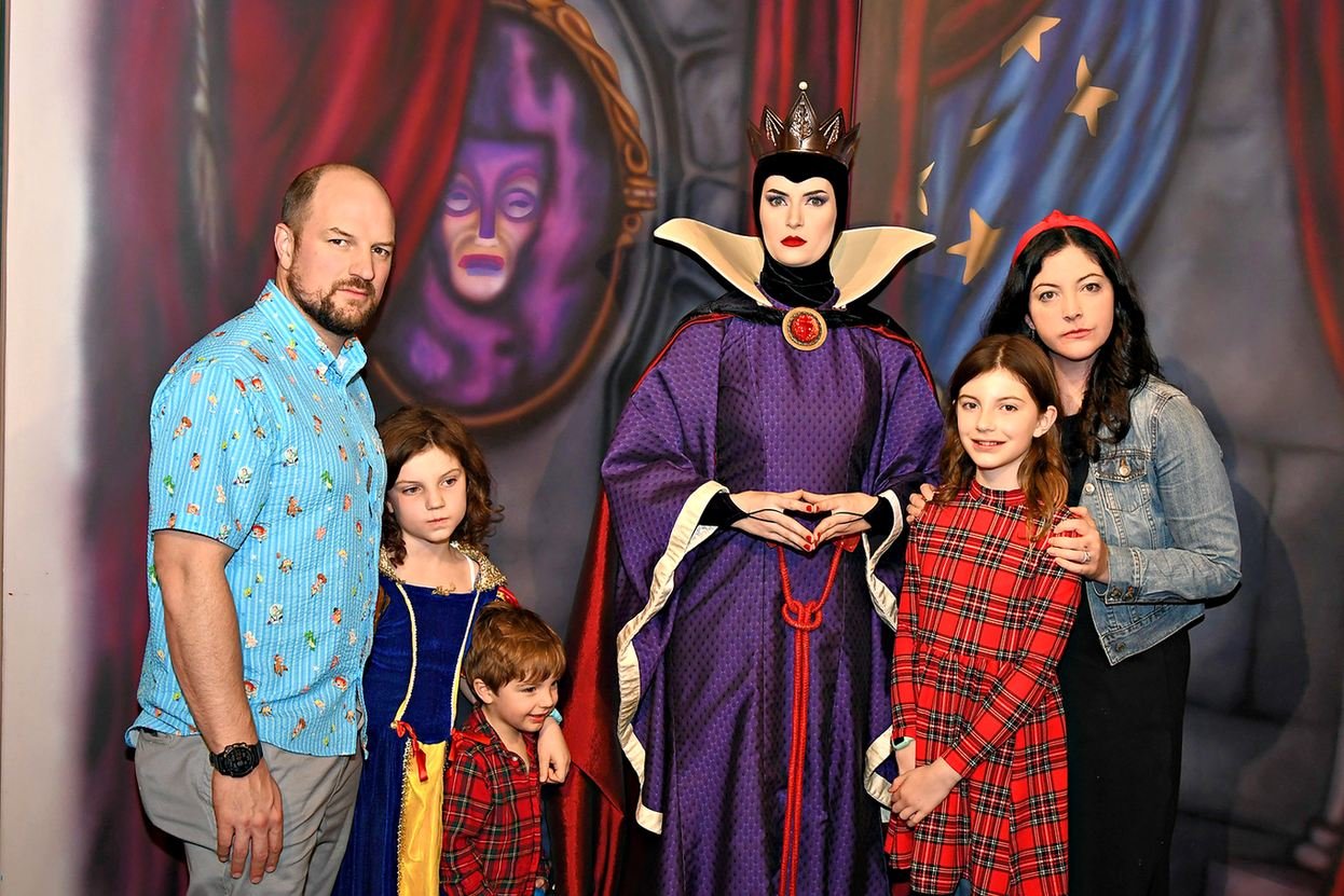 A family of five poses with the Evil Queen at Story Book Dining at Artist Point, a Disney World character dining experience. The dad, the mom, and one daughter pose angry while the other two smile.