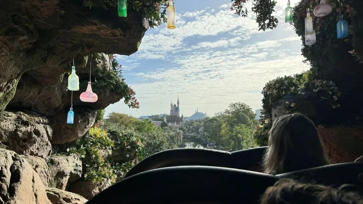 At the top of a cave before the log flume drop in tianas bayou adventure in magic kingdom at disney world. You can see Cinderella's castle and space mountain in the distance, and decorative bottles hanging from cave ceiling.