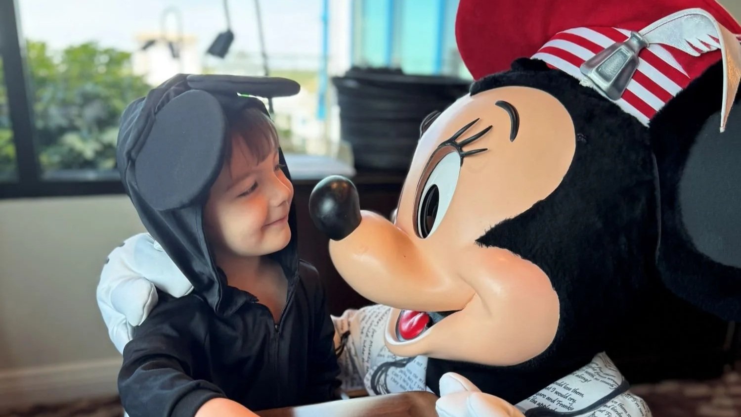 A small boy in a Mickey costume goes nose to nose with Minnie Mouse in her poet's costume at Topolino's Terrace character breakfast, a Disney World character dining experience in the Riviera Resort.