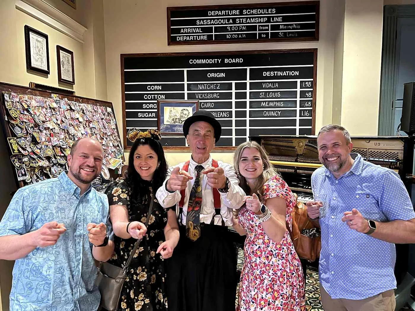 4 adults pose with Yehaa bob at River Roost at Disney's Port Orleans Riverside. They are all pointing at the camera. There's a fake steamship calendar on the wall behind them.