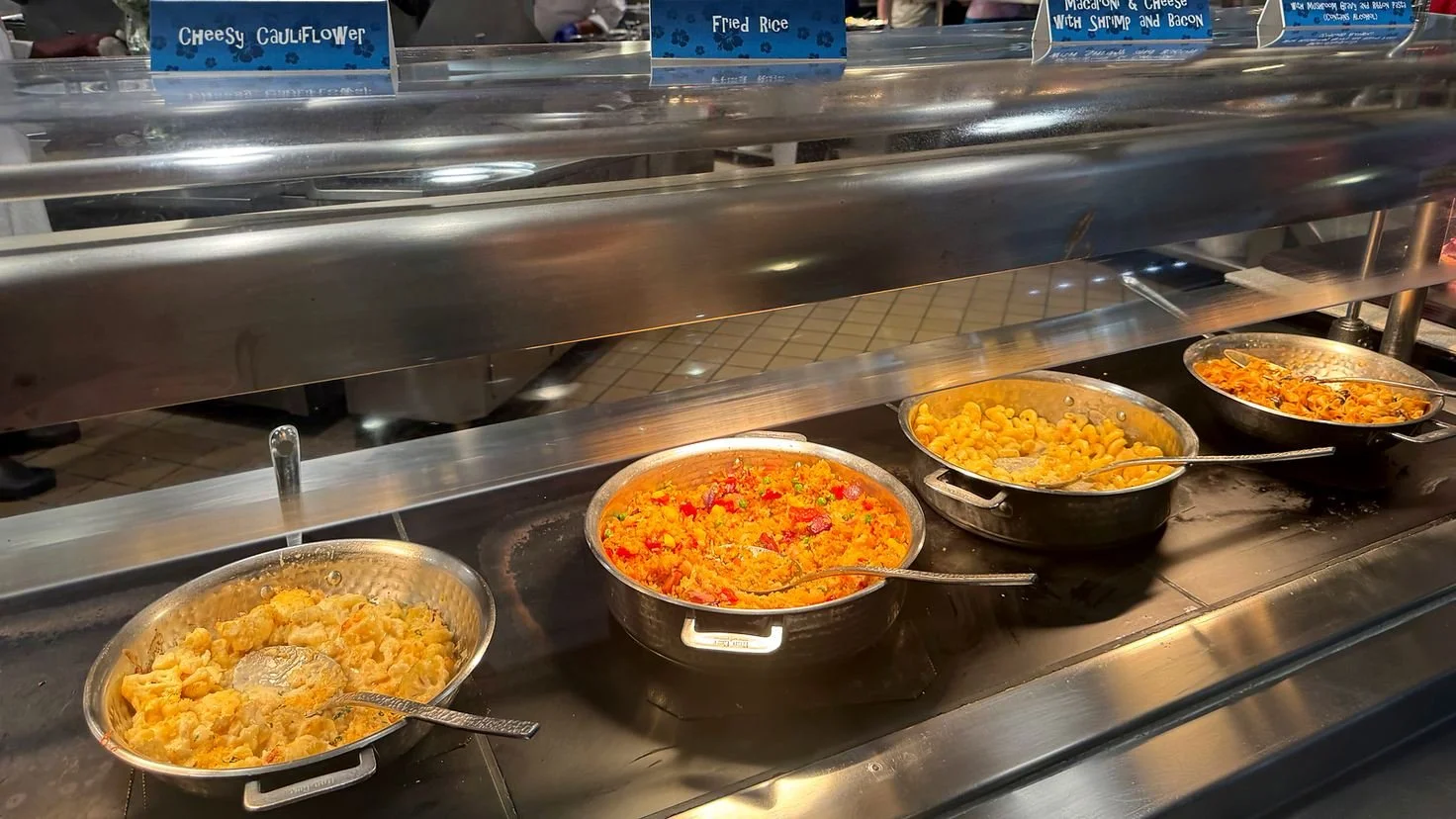 A photograph of four buffet dishes in a stainless steel buffet with sneeze guard. The labels say cheesy cauliflower, rice, mac and cheese with shrimp and bacon. At Hollywood and Vine in Hollywood Studios.