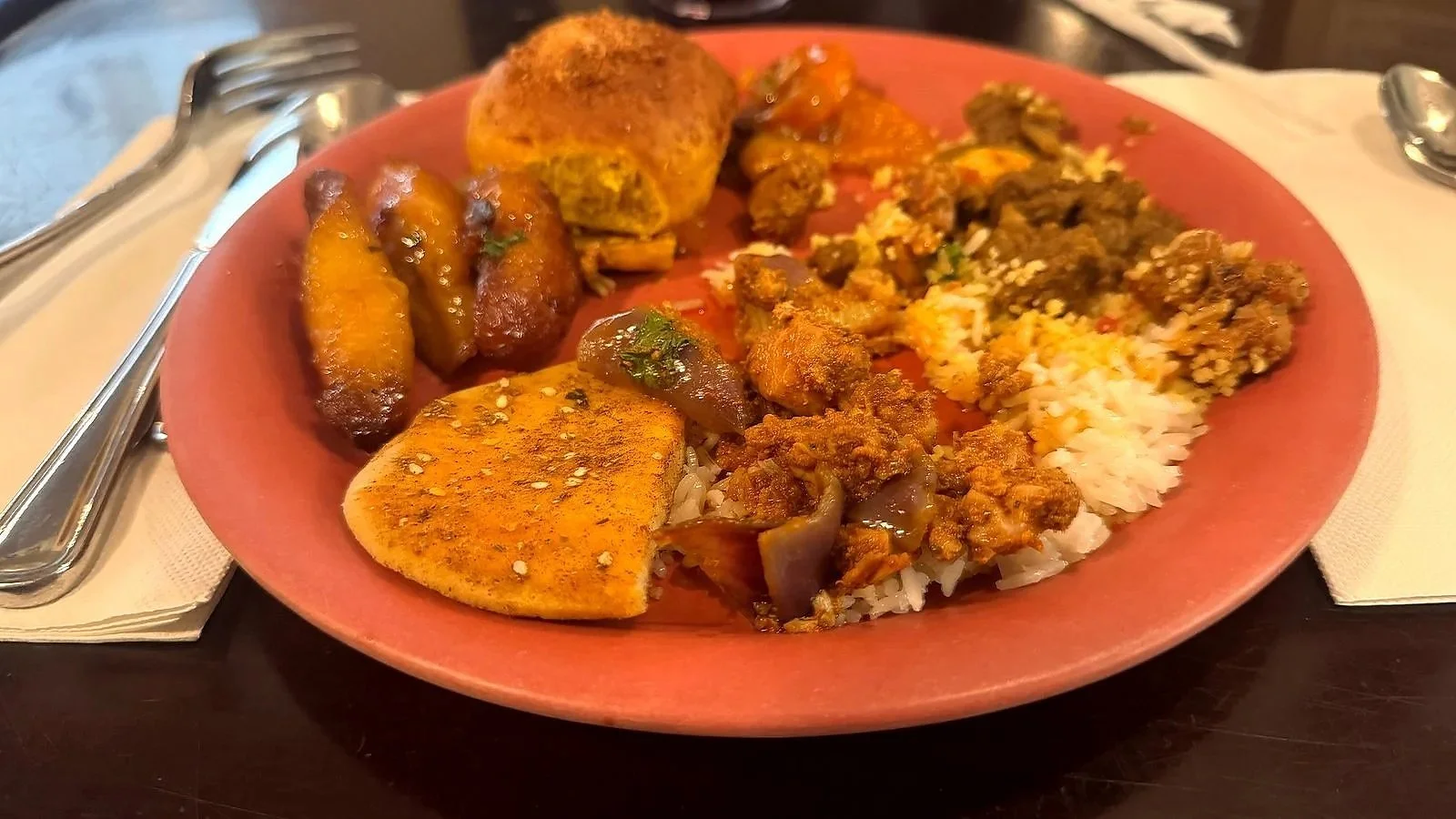 A pink plate with a variety of exotic food, including curry rice, friend plantains, and other African-inspired food. At Tusker House, a character meal in the Africa section of Animal kingdom.