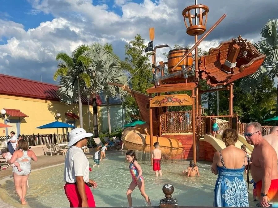 A large play structure at the pool at Caribbean Beach Resort in Disney World, a moderate resort. It's shaped like a wrecked ship and has multiple water features and water slides.