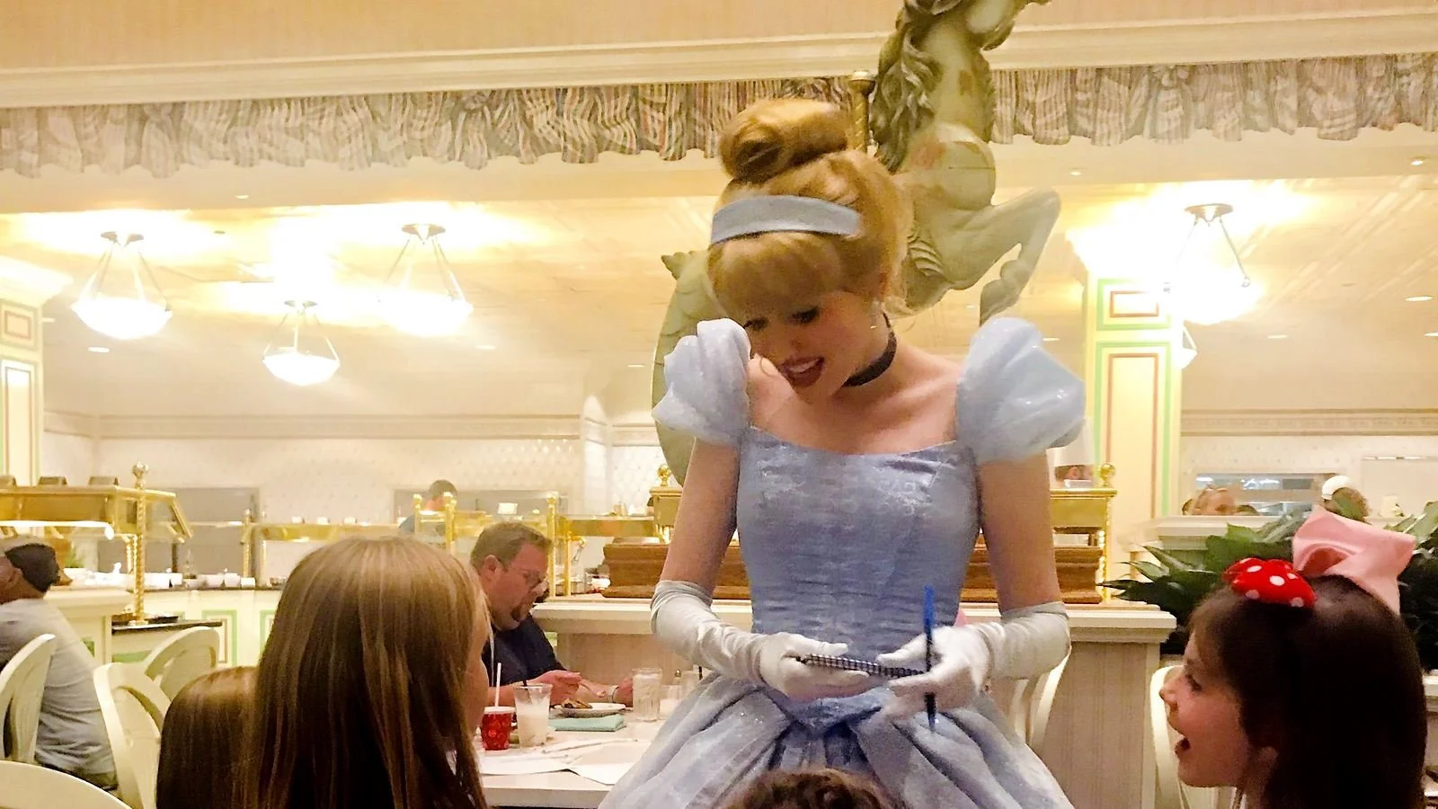 Cinderella talks to several young girls as she signs autographs. You can see the gold buffet stations behind her. At 1900 Park Fare, a Disney World character dining restaurant.