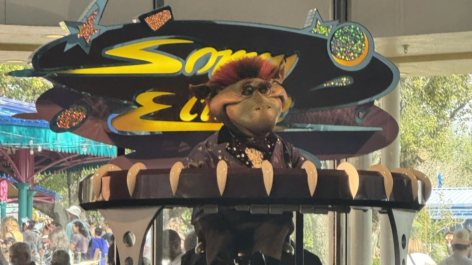 The animatronic alien at Cosmic Ray's, Sonny Eclipse looks like a lizard with orange hair and a tuxedo. He's playing a paino with his name behind him. At Magic Kingdom. Fun fast food for kids at Disney World.