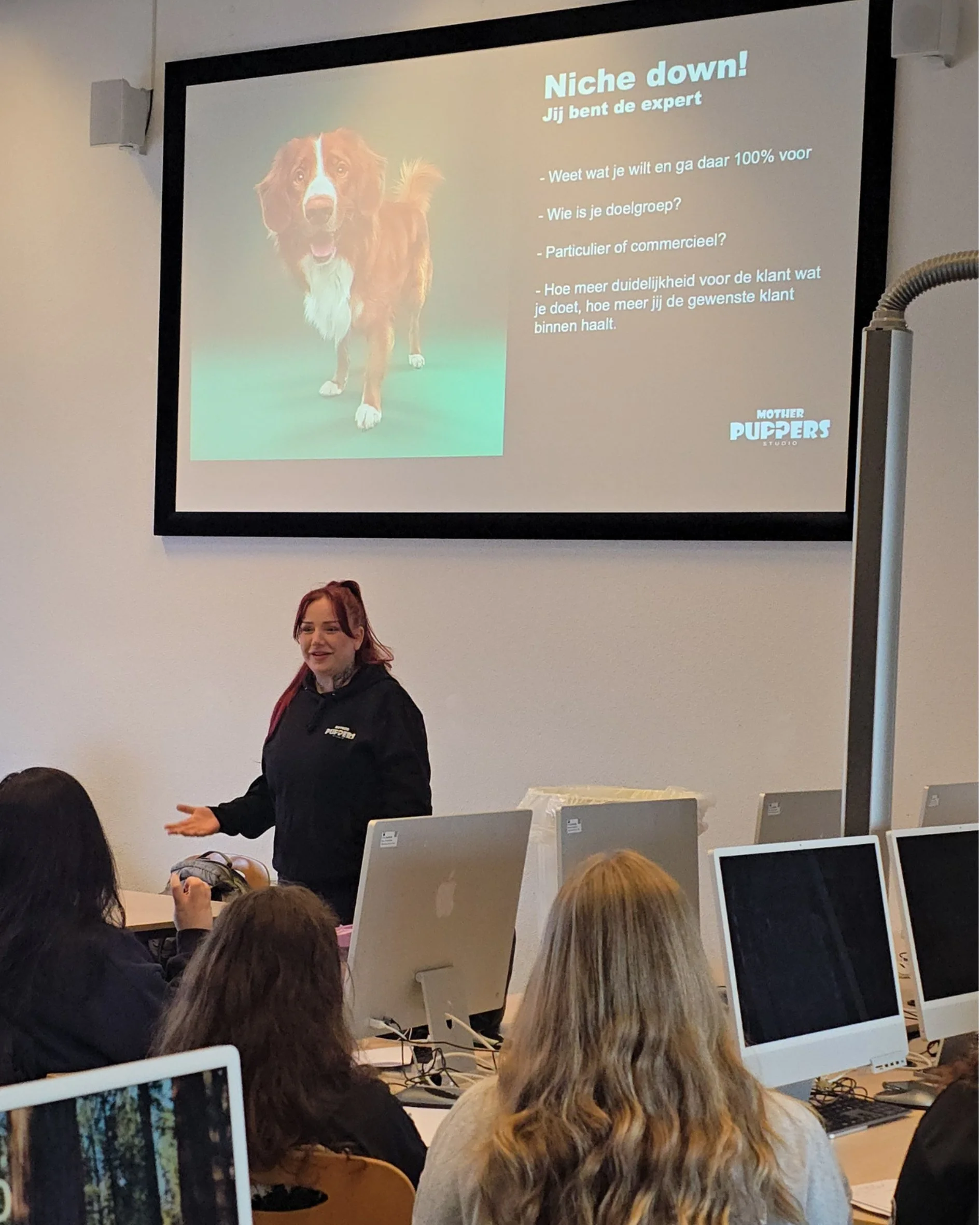 Een presentatie in een klaslokaal met een slide over het promoten van een nichemarkt, met een afbeelding van een hond en een instructie voor het identificeren van de doelgroep.