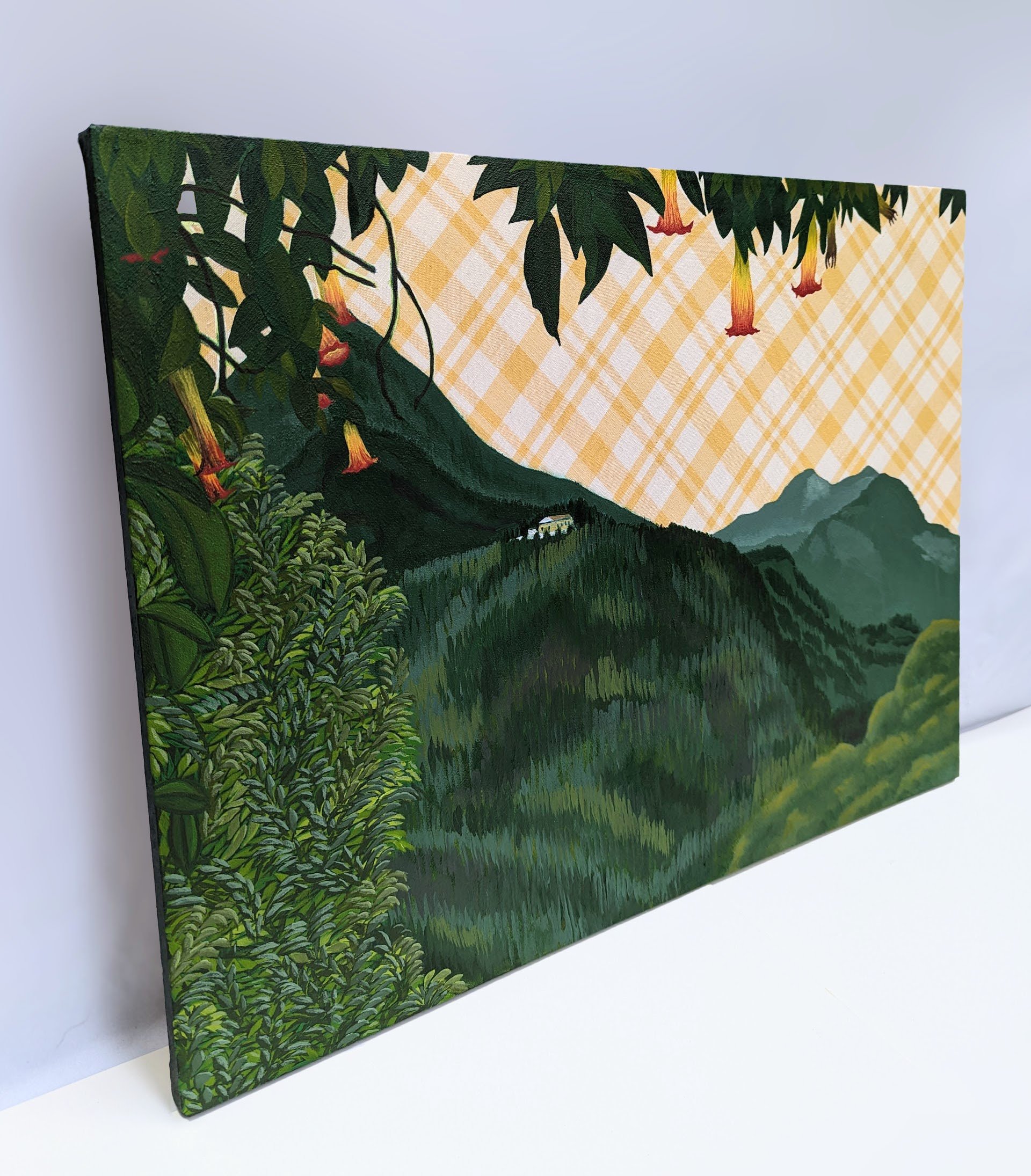 A side view of a landscape painting. The sky is the fabric the artwork is  painted on, a yellow and white plaid material. A white house is in the distance on green mountains and trumpet flowers hang from the top of the image.
