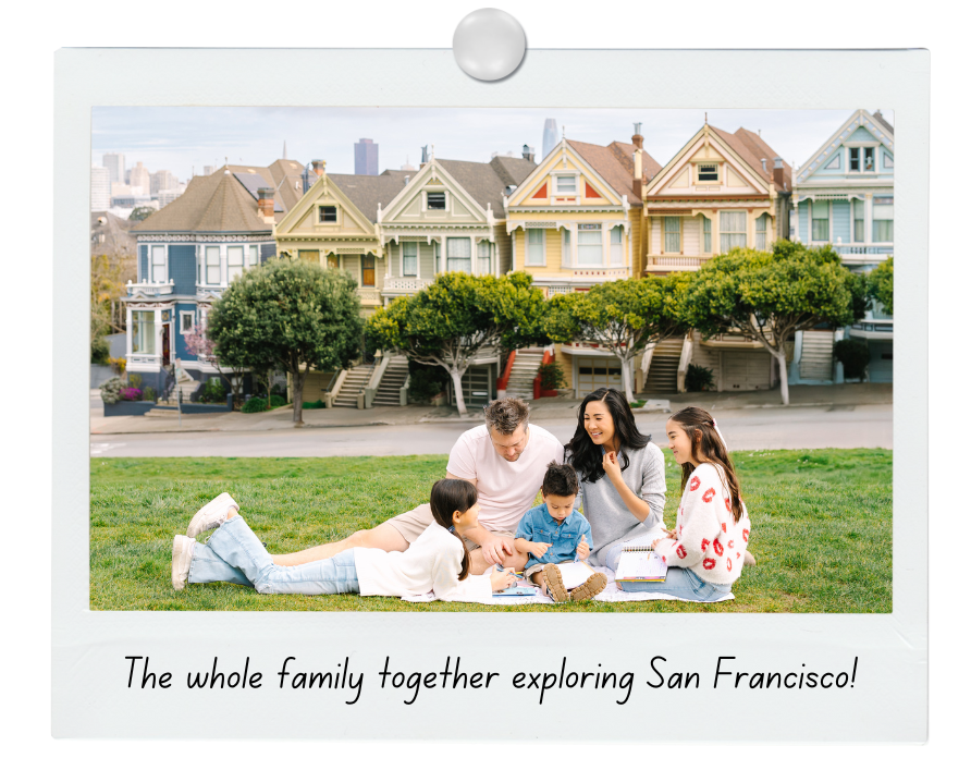 Family sitting on grass in front of colorful Victorian houses in San Francisco, enjoying a day together.