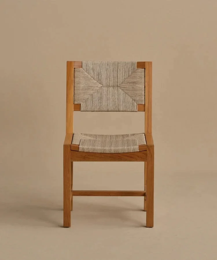 Natural teak outdoor dining chair with a handwoven rope seat and geometric woven back, photographed against a warm neutral background.